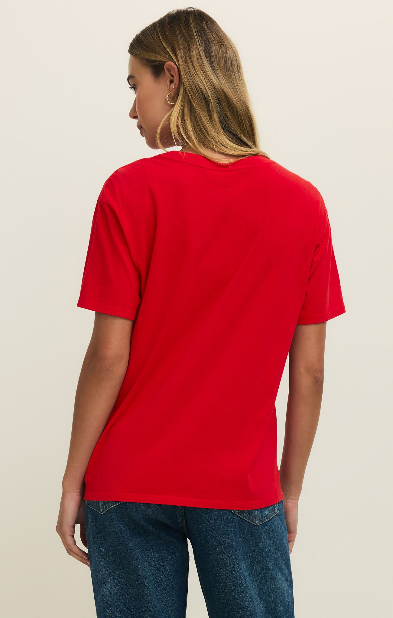 Person wearing a red t-shirt and blue jeans on a beige background
