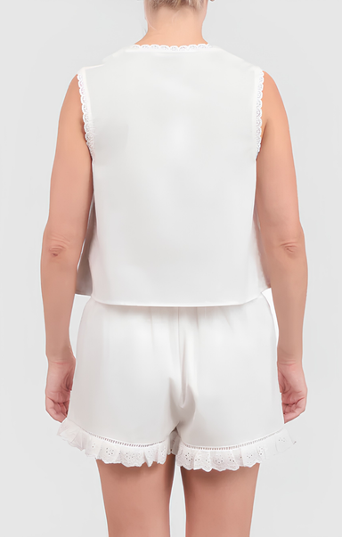Person wearing a white sleeveless top and shorts with lace trim on a plain background