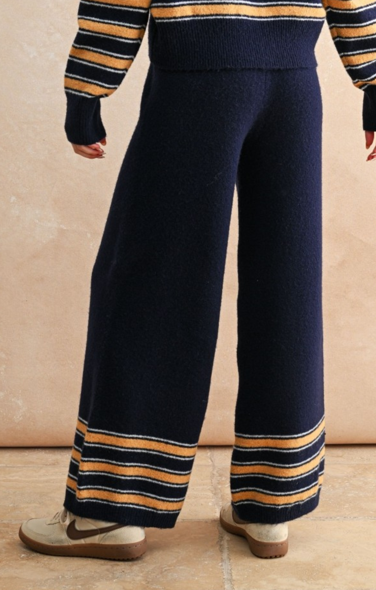 Navy blue pants with yellow and black stripes worn by a person on a beige background