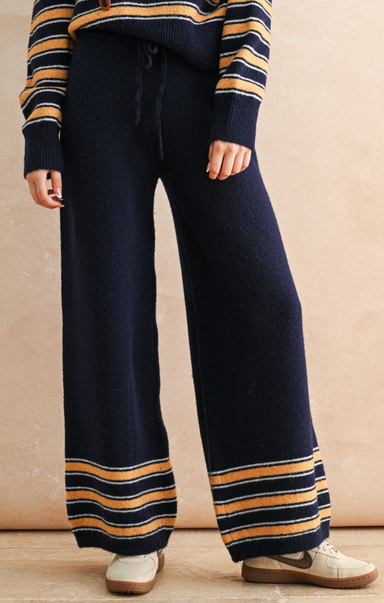 Navy blue pants with yellow stripes worn by a person against a beige background