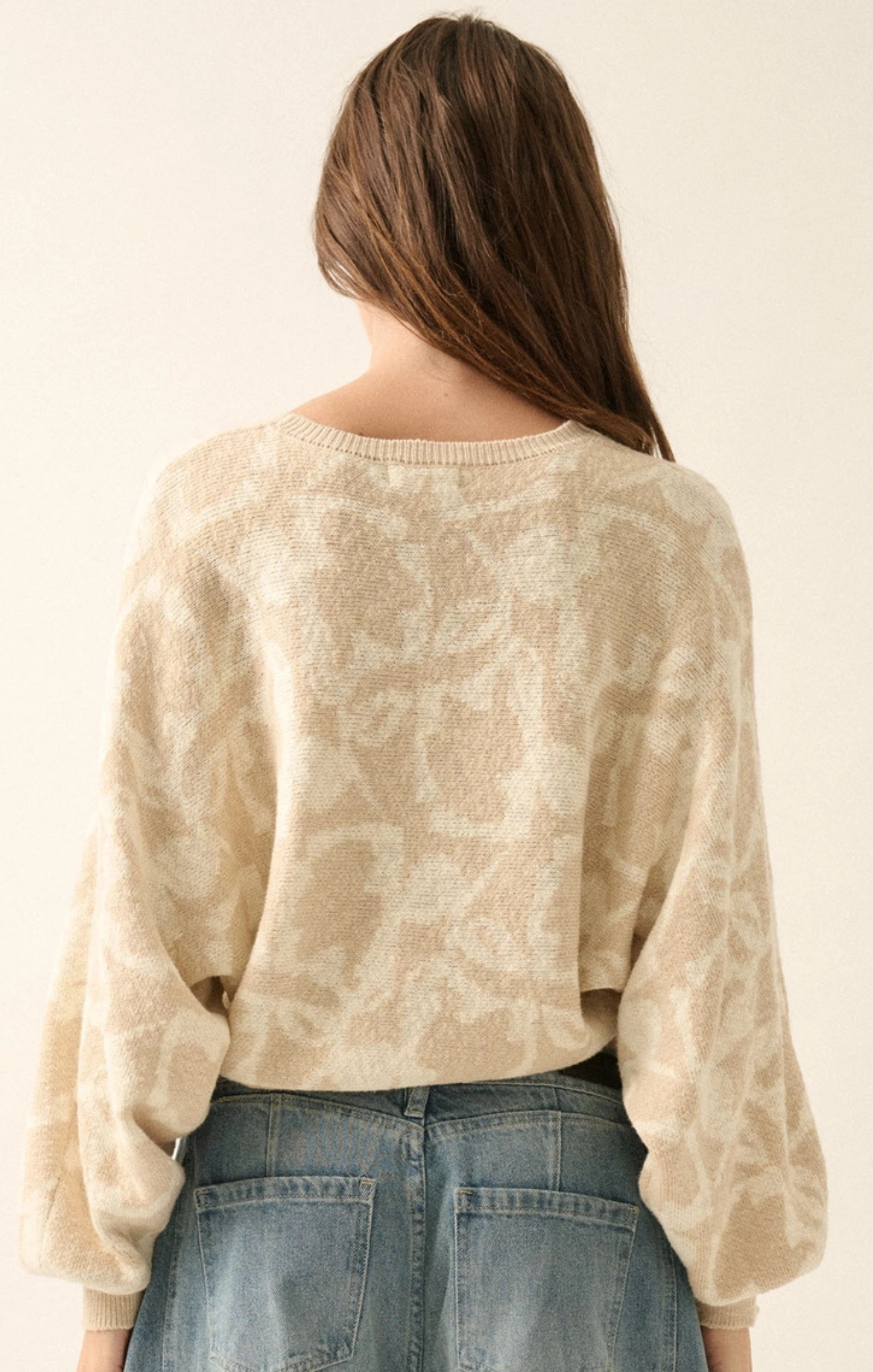 Person wearing a beige sweater and blue jeans against a plain background