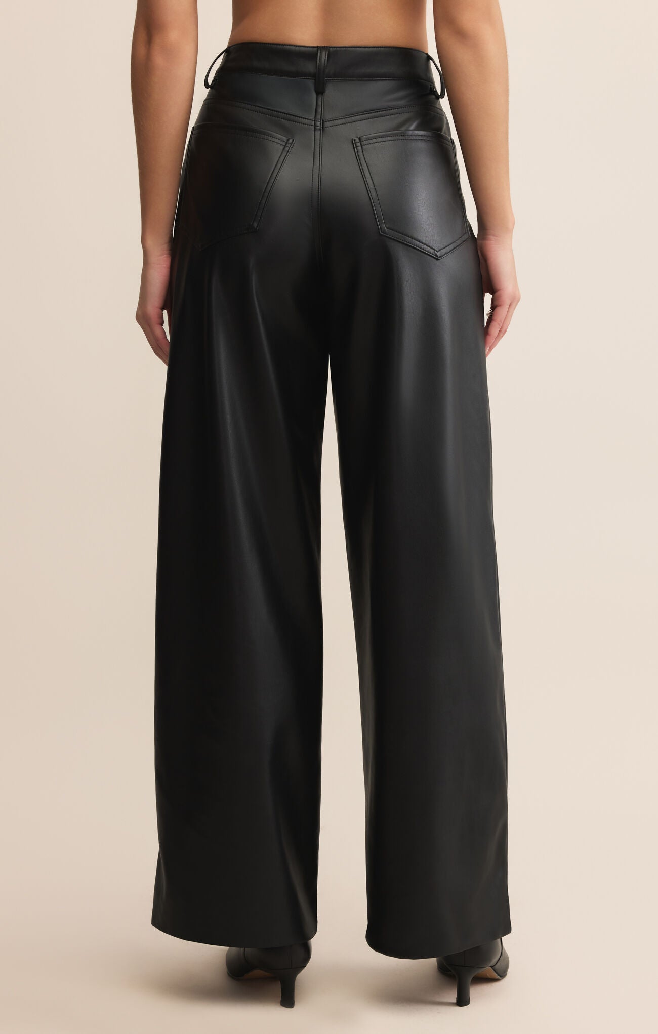Black leather wide-leg pants worn by a person on a beige background