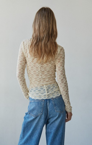 Person wearing a beige lace top and blue jeans against a plain background