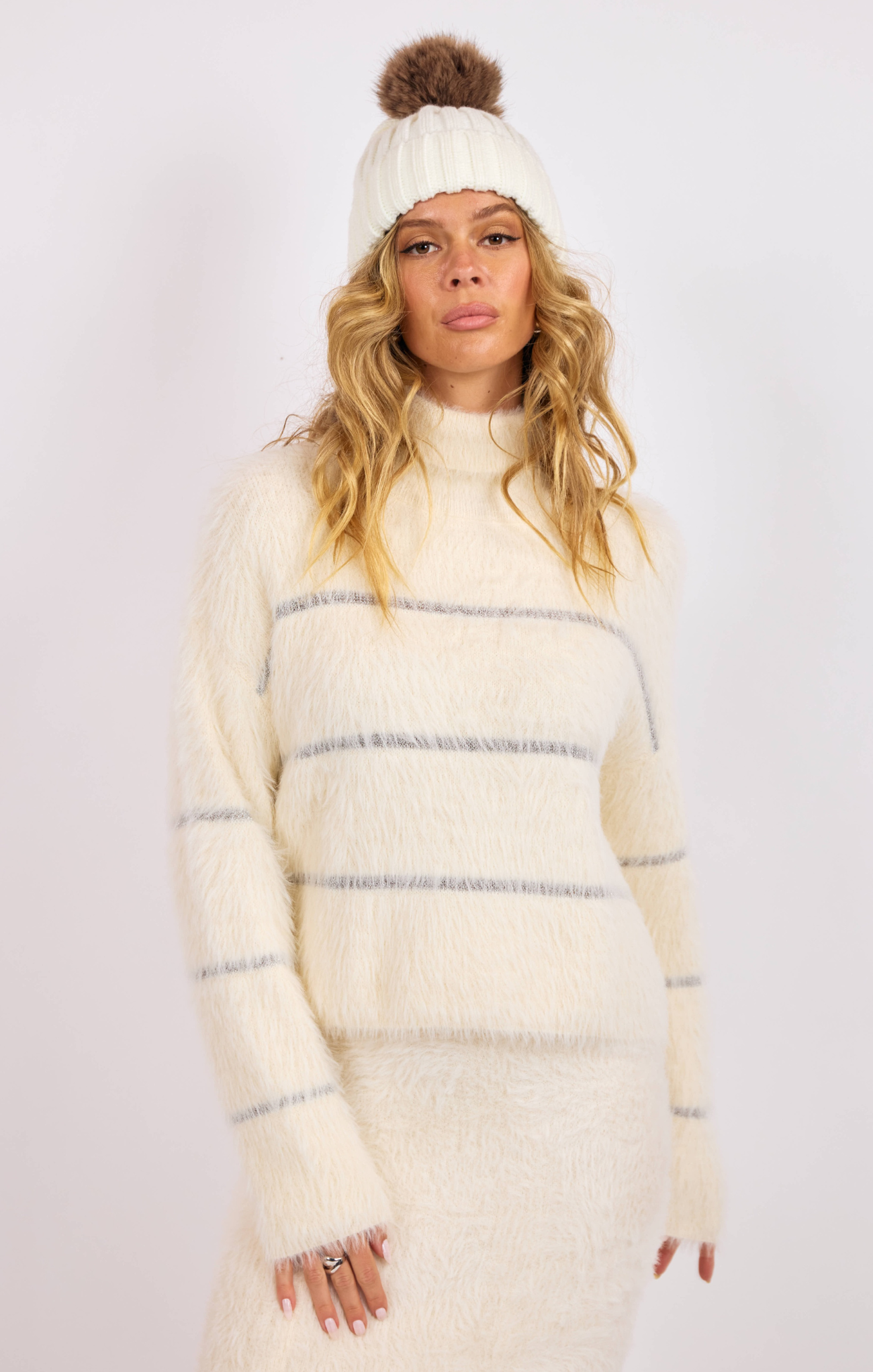 Woman wearing a cream-colored knit outfit with a matching beanie on a white background