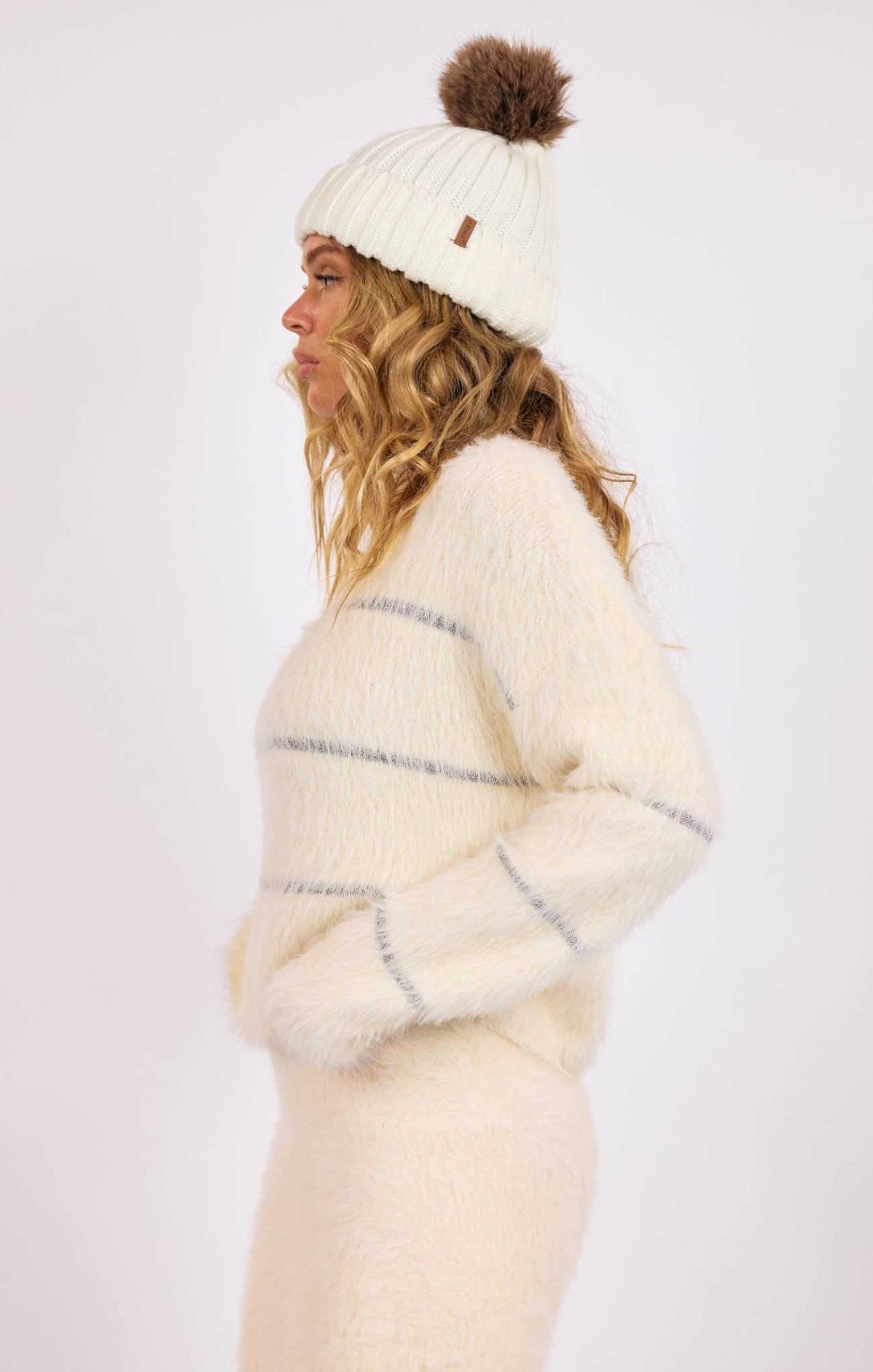 Woman wearing a cream-colored knit sweater and hat with a pom-pom on a white background