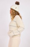 Woman wearing a cream-colored knit sweater and hat with a pom-pom on a white background