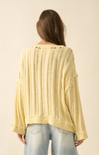 Light yellow cable knit sweater worn by a person on a beige background