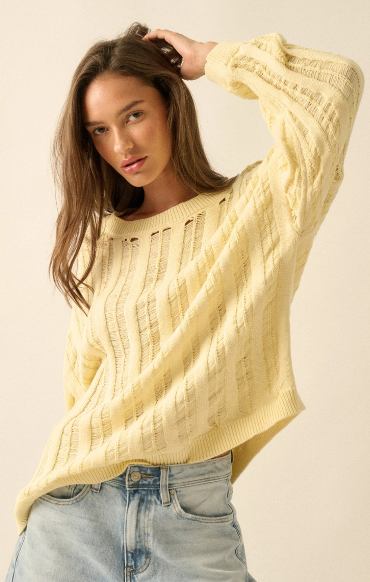 Woman wearing a yellow sweater and blue jeans against a beige background