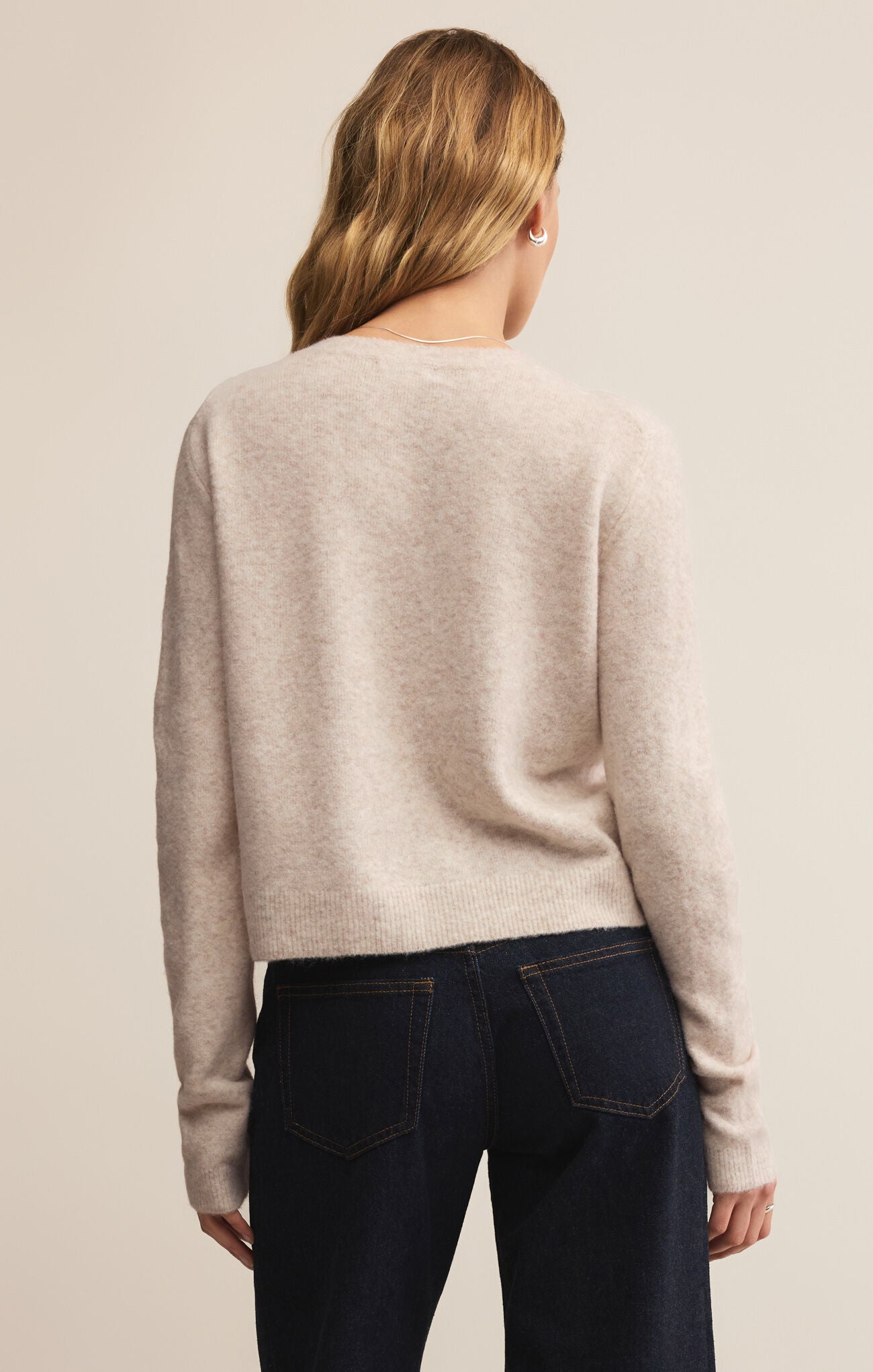 Person wearing a beige sweater and dark jeans on a plain background