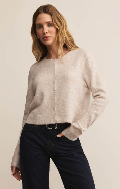 Woman wearing a light gray sweater and dark jeans against a plain background