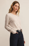 Woman wearing a beige sweater and dark jeans against a plain background