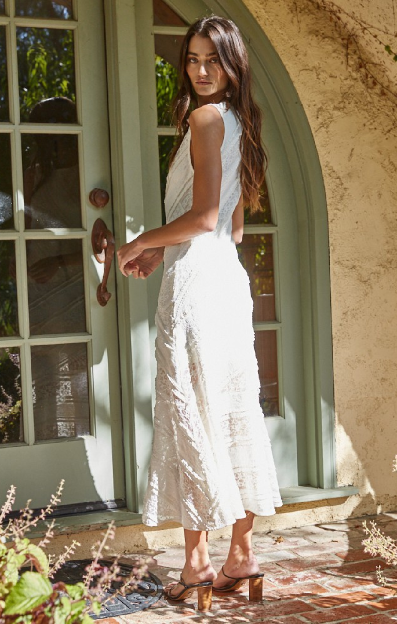 Woman in a white dress standing in front of a door with an archway.