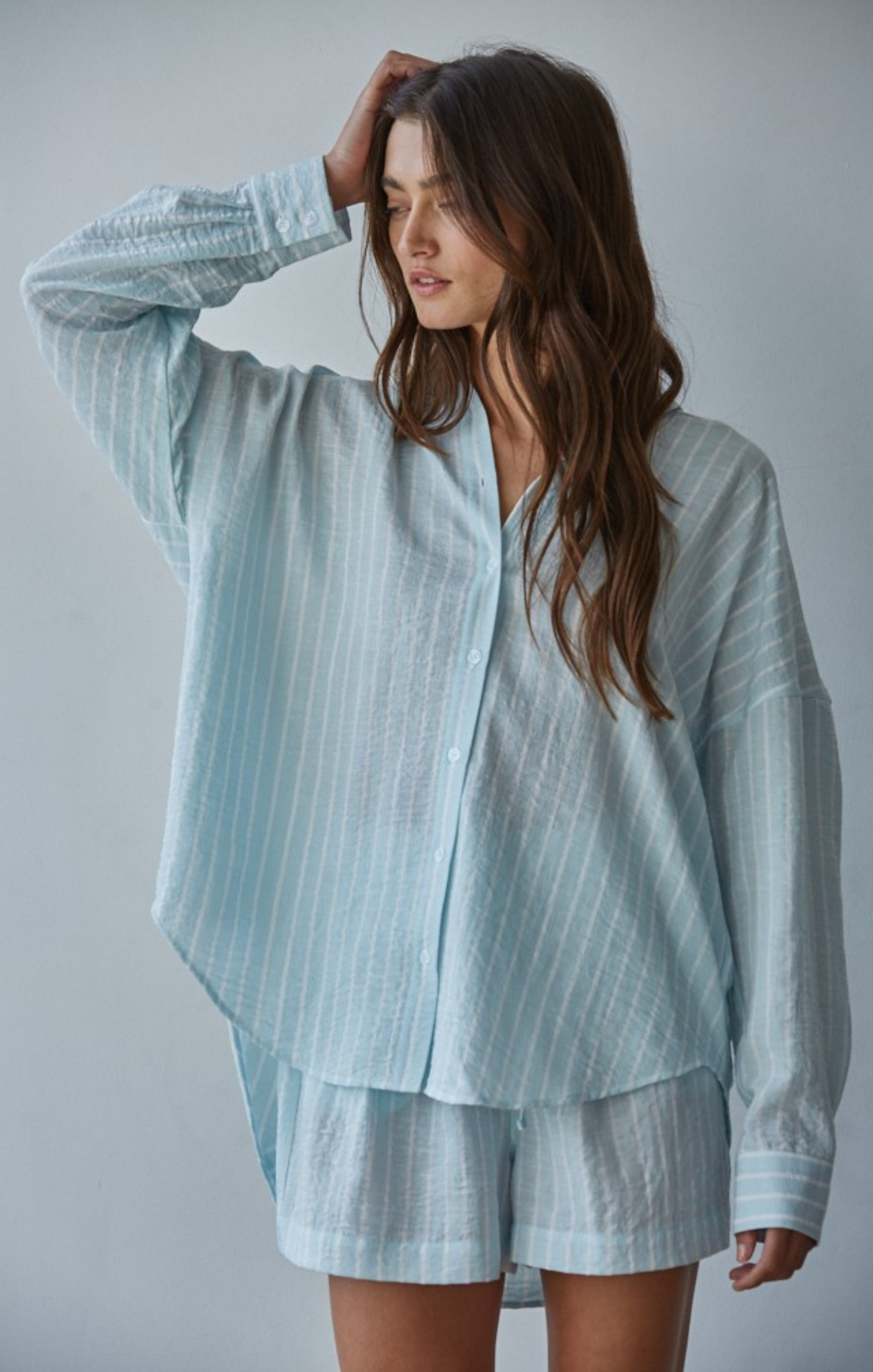 Woman wearing a light blue striped shirt and shorts set against a plain background