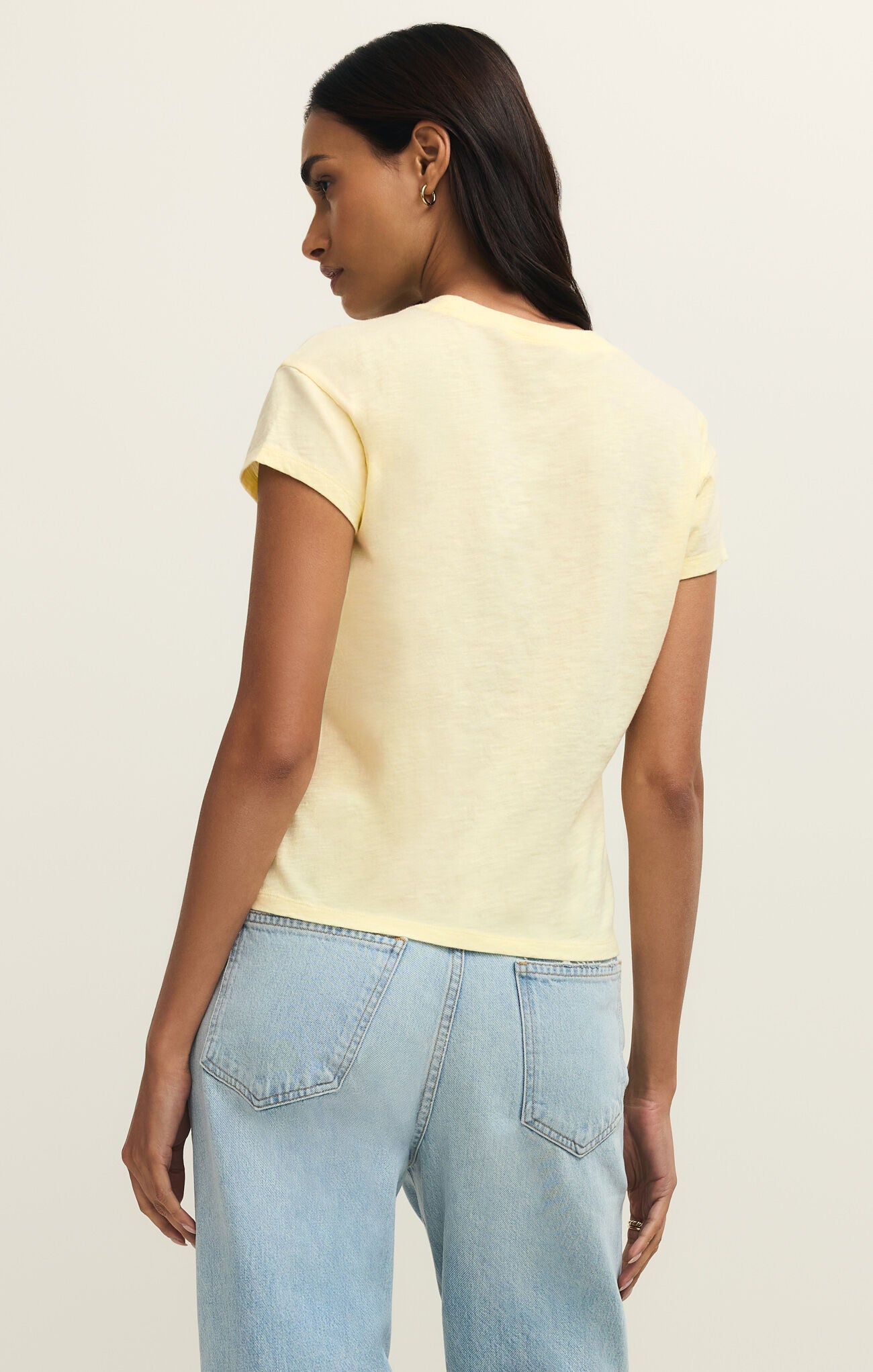 Woman wearing a yellow top and light blue jeans on a beige background