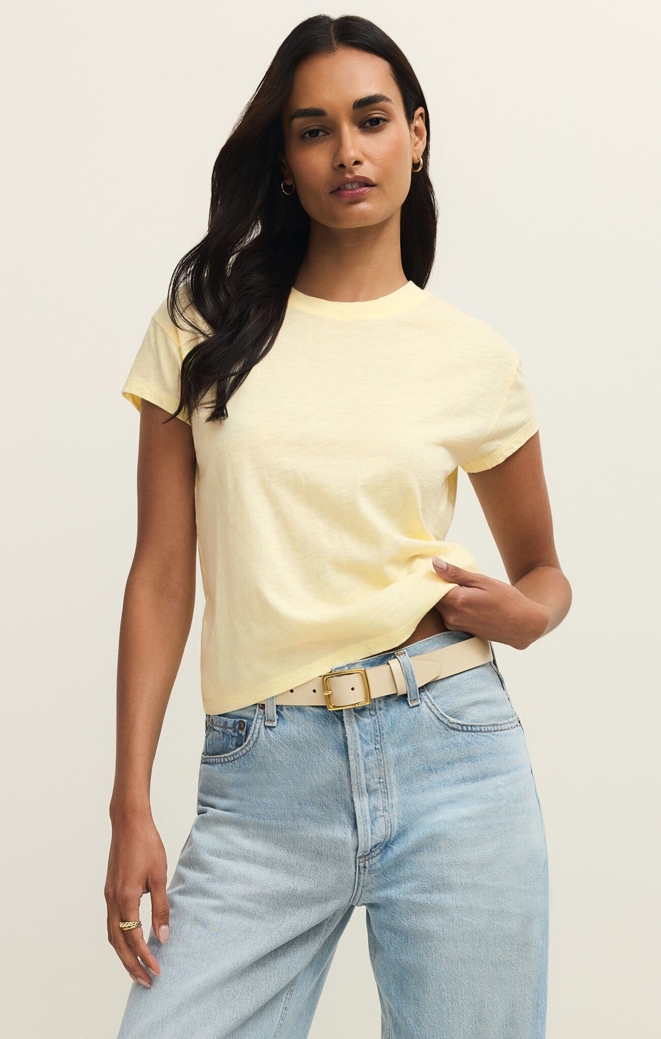 Woman wearing a yellow t-shirt and light blue jeans against a plain background