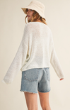 Person wearing a white sweater and denim shorts with a beige hat on a plain background