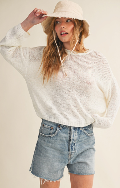Woman wearing a white sweater and denim shorts with a beige hat on a plain background