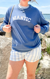 Person wearing a blue sweatshirt with 'Niantic' text and checkered shorts by the ocean.