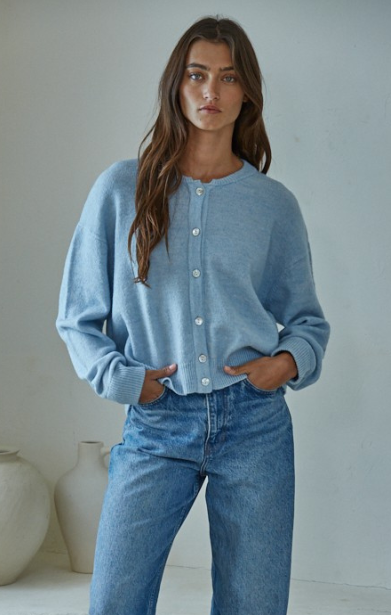Woman wearing a light blue cardigan and jeans against a plain background