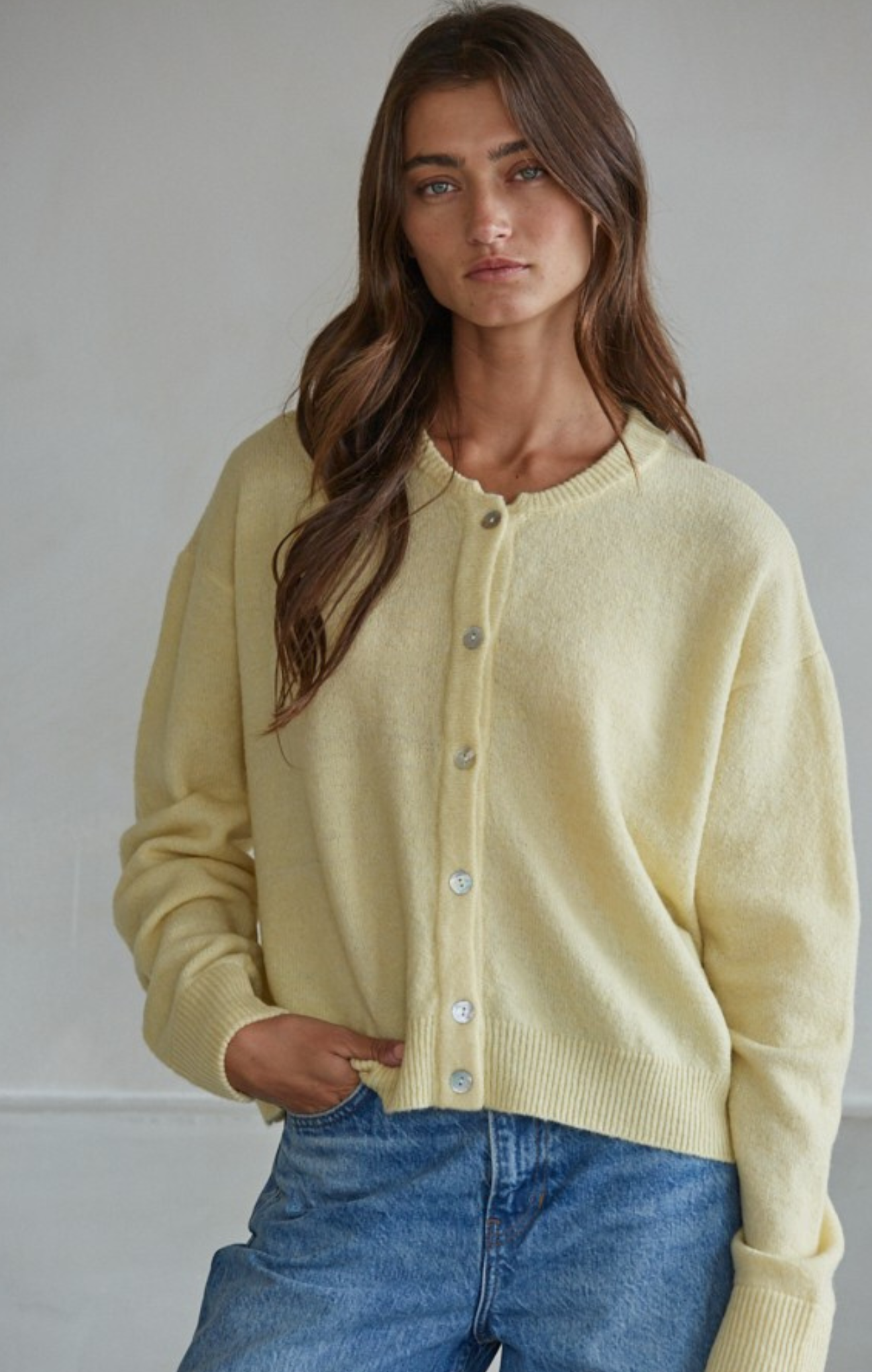 Woman wearing a light yellow cardigan and blue jeans against a plain background