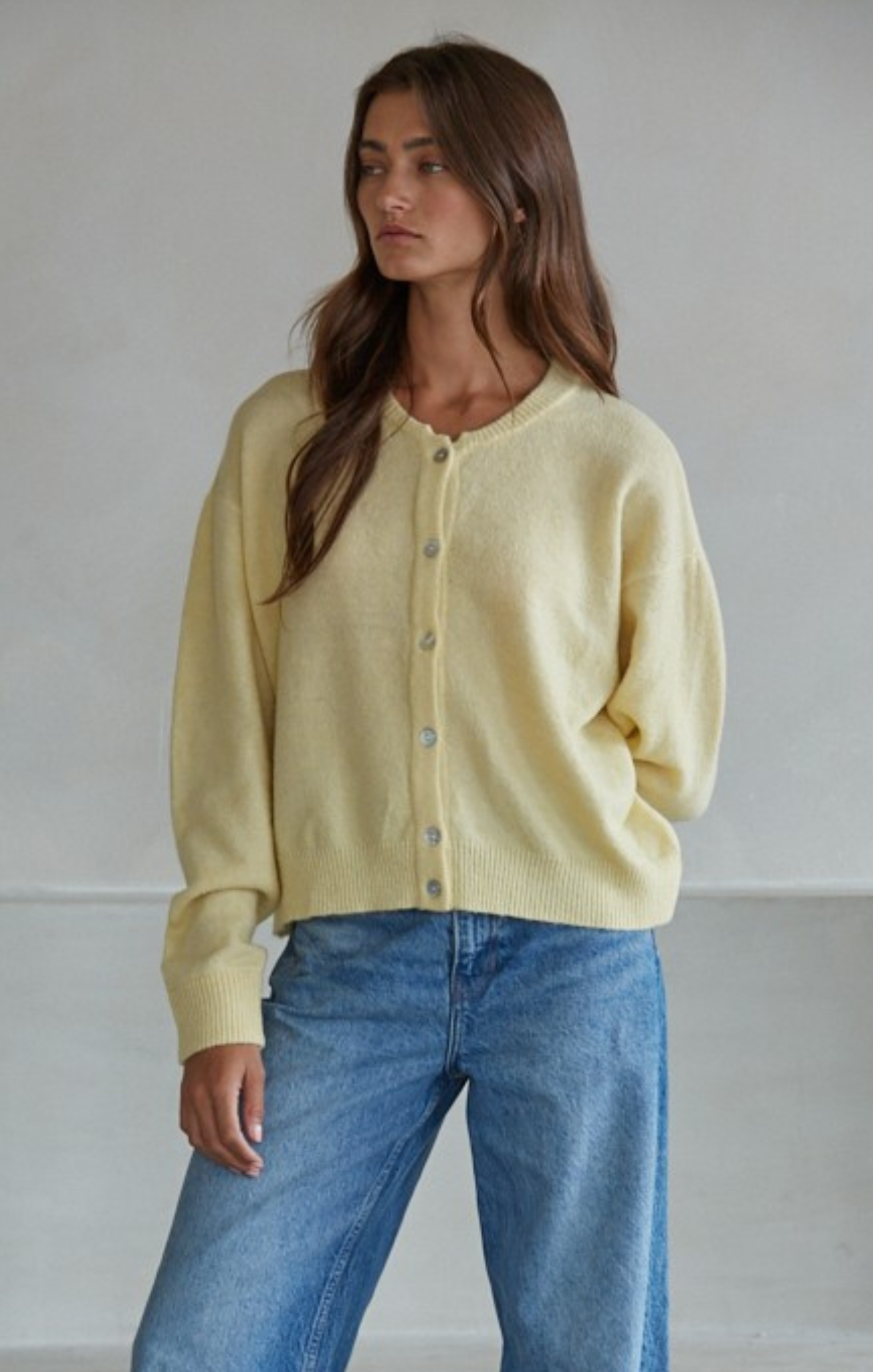 Woman wearing a light yellow cardigan and blue jeans against a plain background