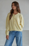 Woman wearing a light yellow cardigan and blue jeans against a plain background