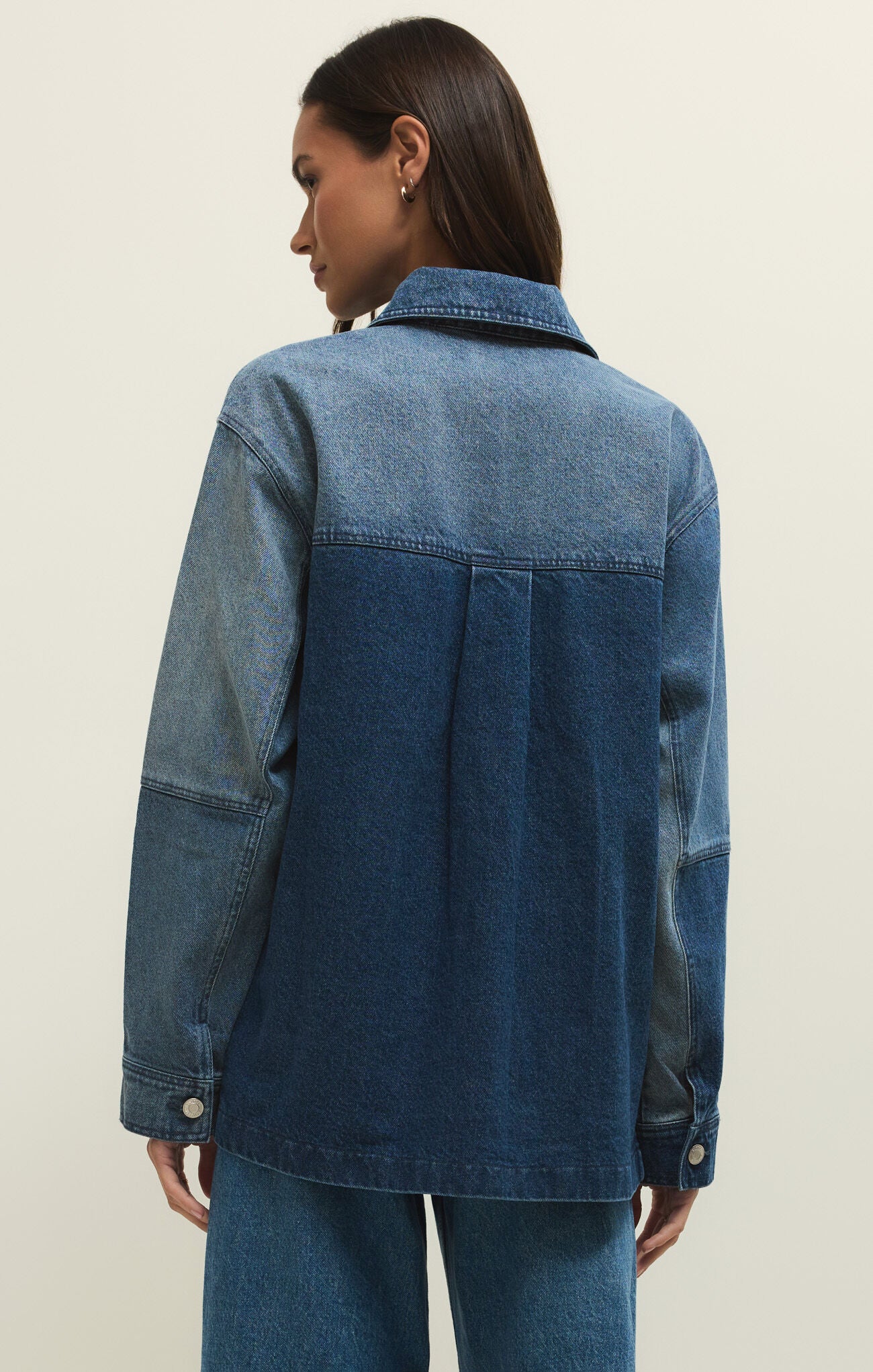 Person wearing a blue denim jacket on a plain background