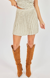 Person wearing a beige pleated skirt and brown knee-high boots on a white background