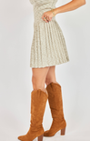 Person wearing a beige pleated skirt and brown knee-high boots on a white background