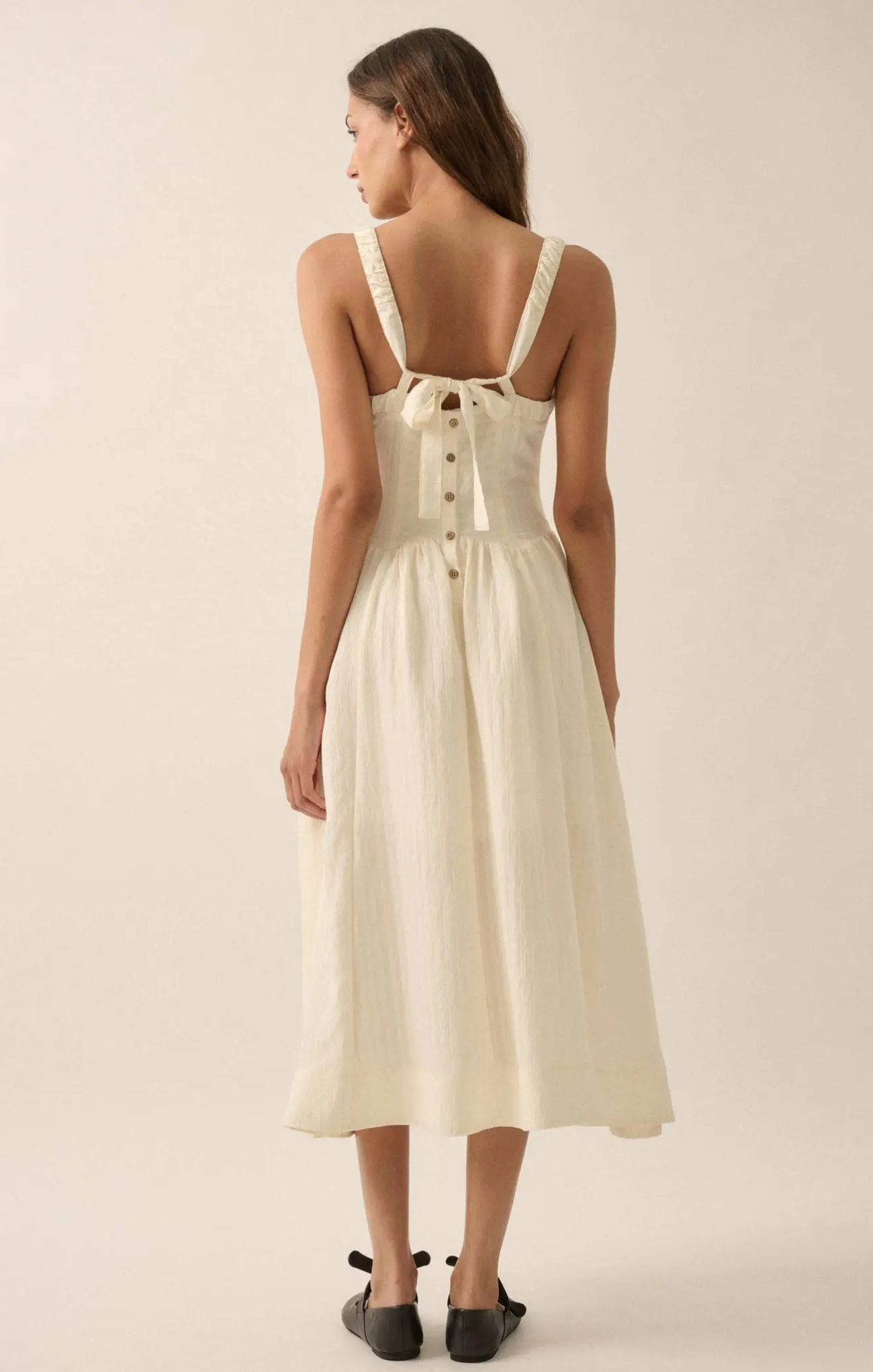 Woman wearing a white dress with button details on a plain background