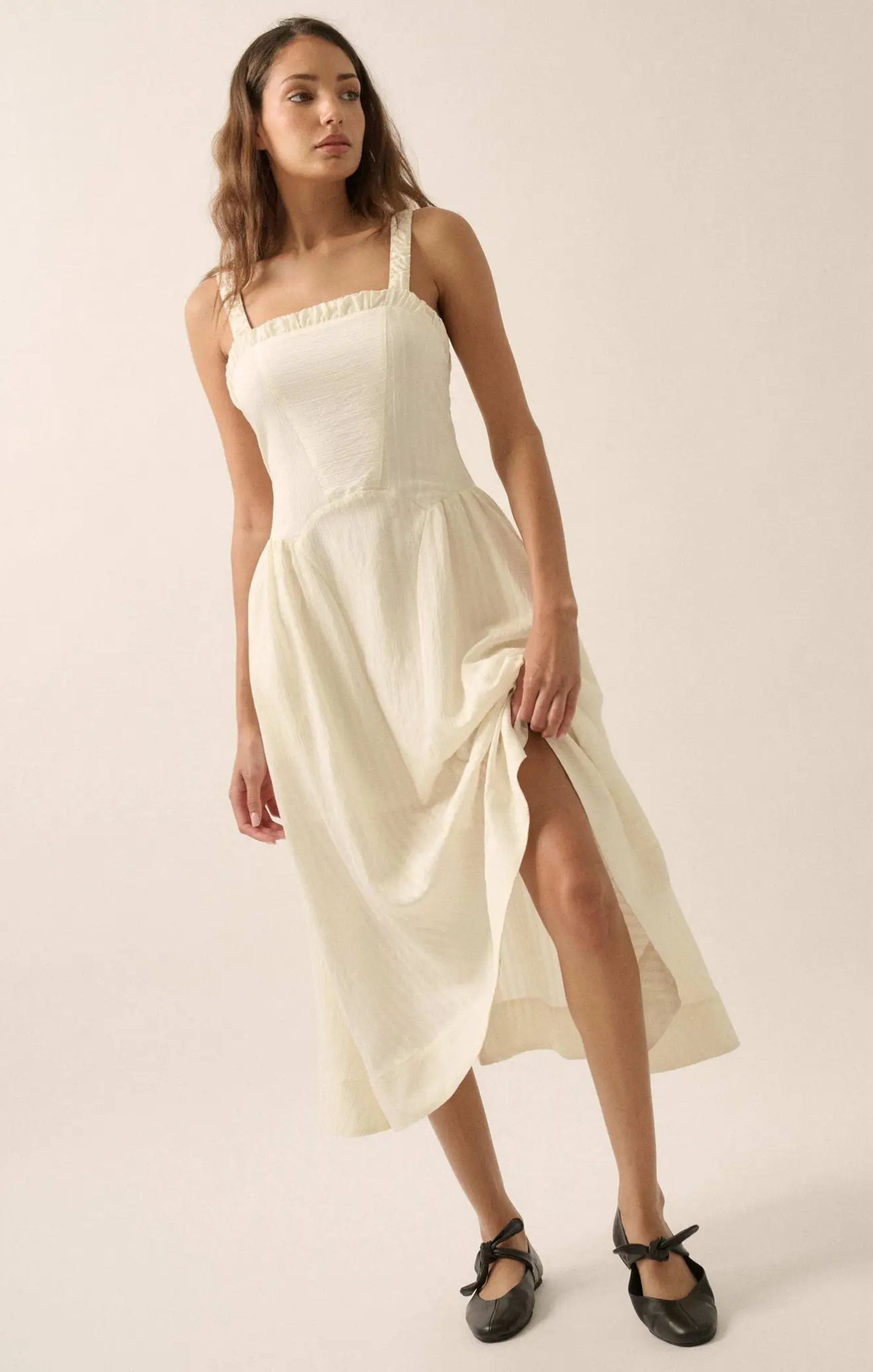 Woman wearing a white dress with a slit on a plain background