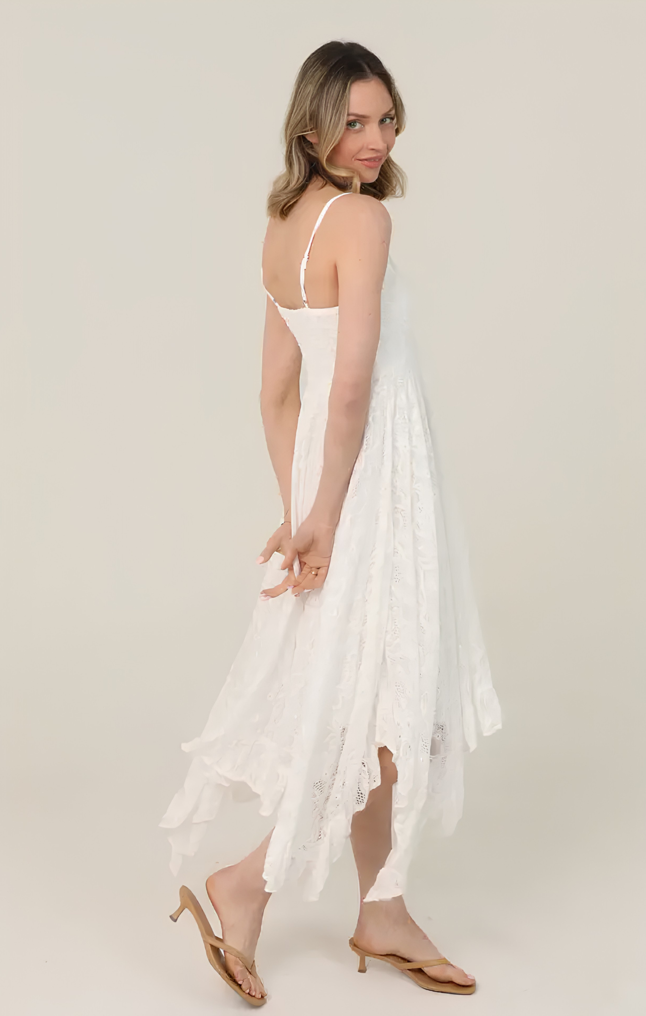 Woman wearing a white dress with thin straps on a plain background