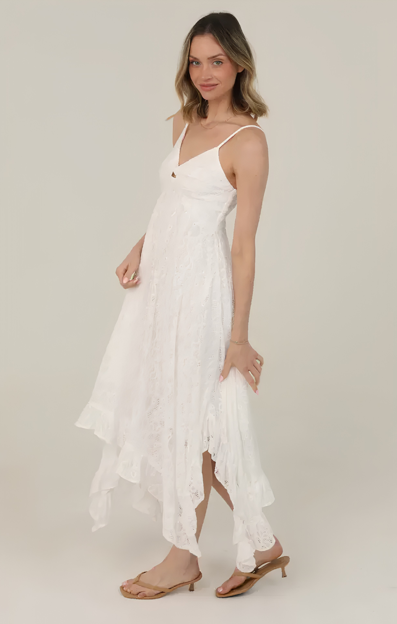Woman wearing a white dress with thin straps on a plain background