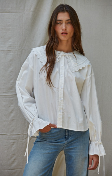 Woman wearing a white blouse with ruffled details and blue jeans against a plain background