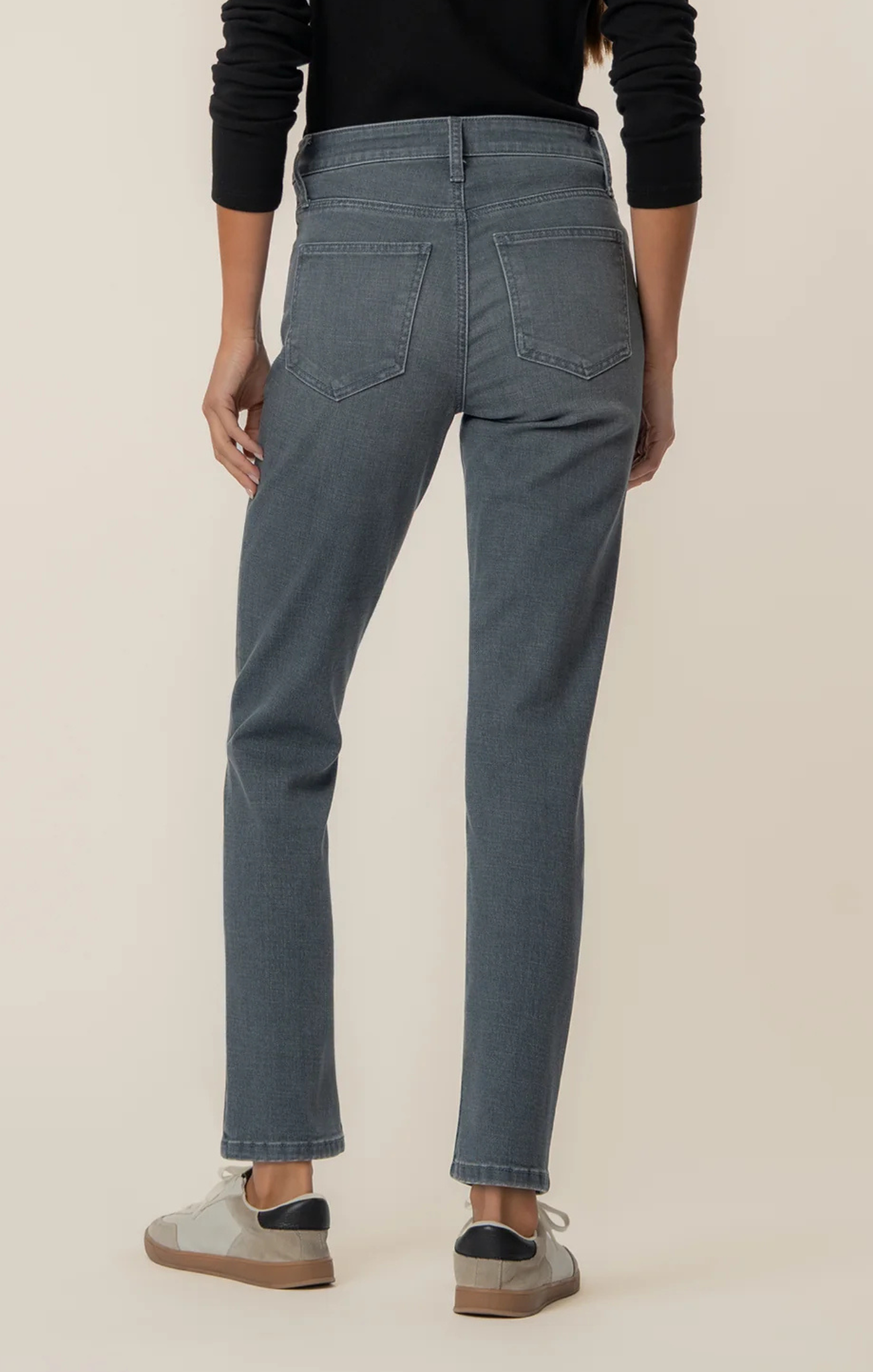 Person wearing mid-wash straight-leg jeans paired with a black long-sleeve top and light gray sneakers, shown from shoulders to feet against a neutral background.