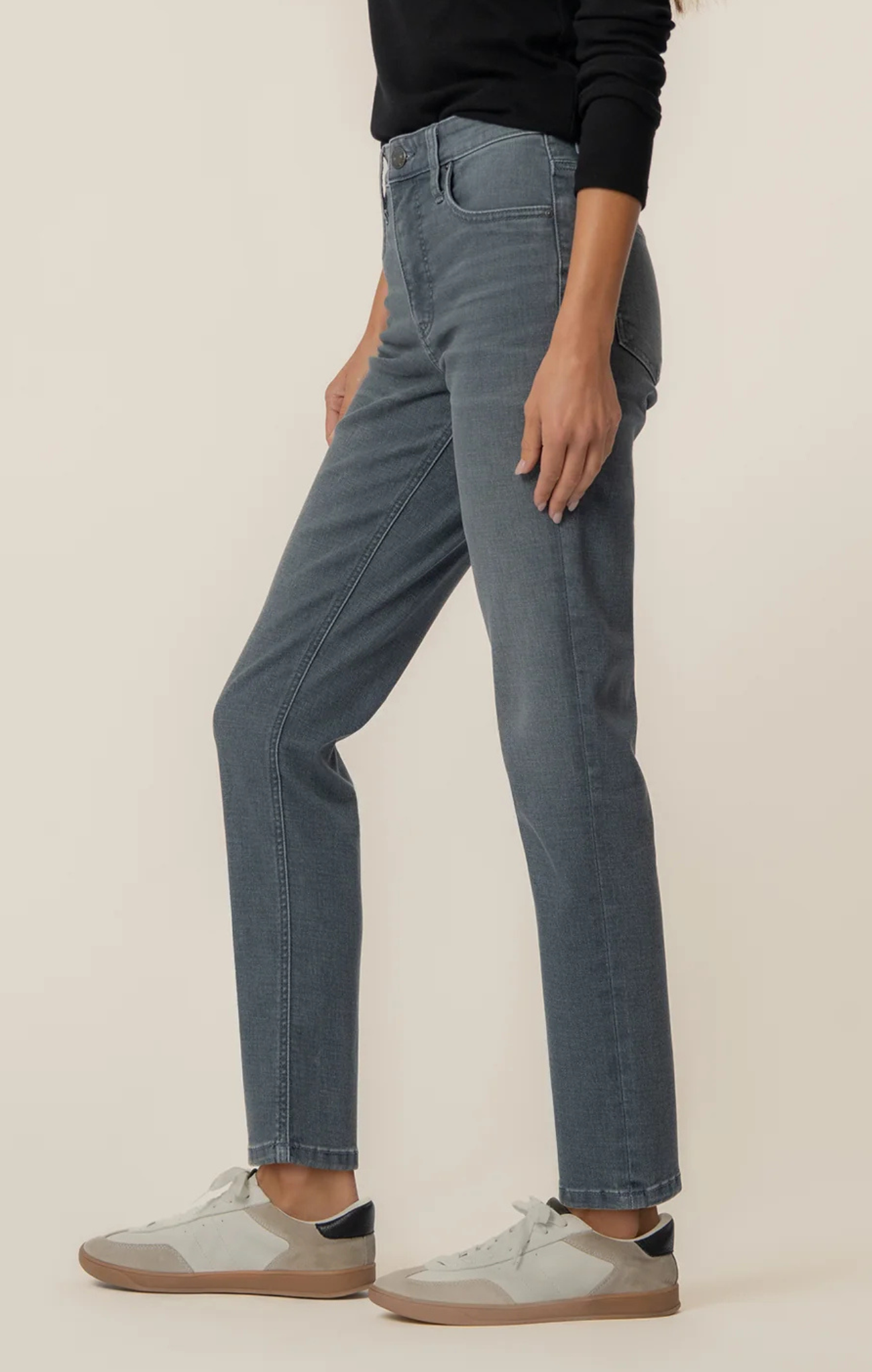 Person wearing mid-wash straight-leg jeans paired with a black long-sleeve top and light gray sneakers, shown from shoulders to feet against a neutral background.