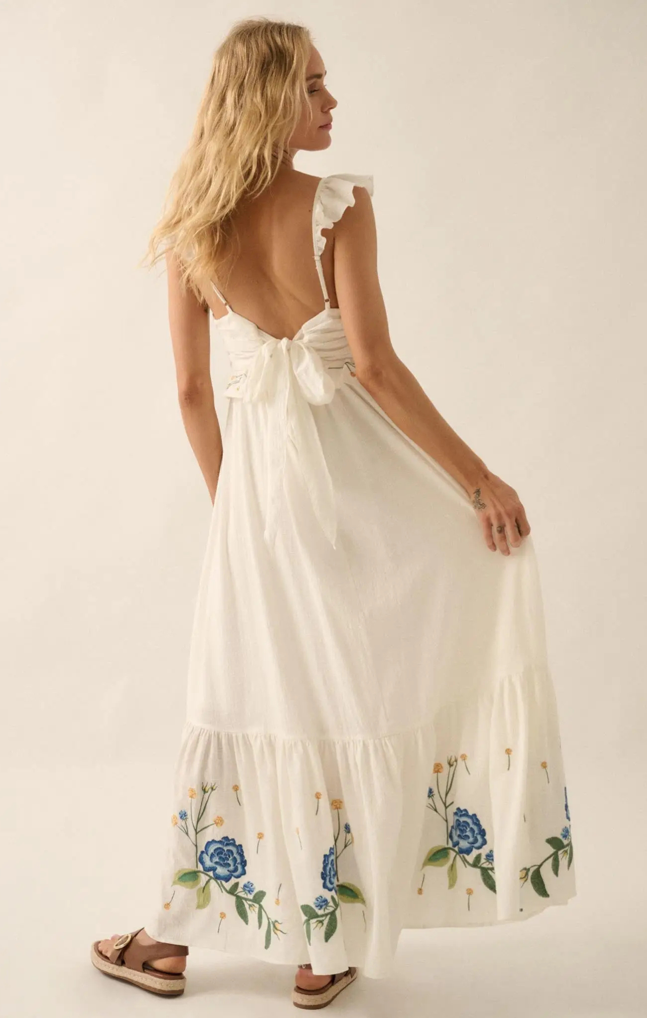 Woman wearing a white dress with floral embroidery on a plain background