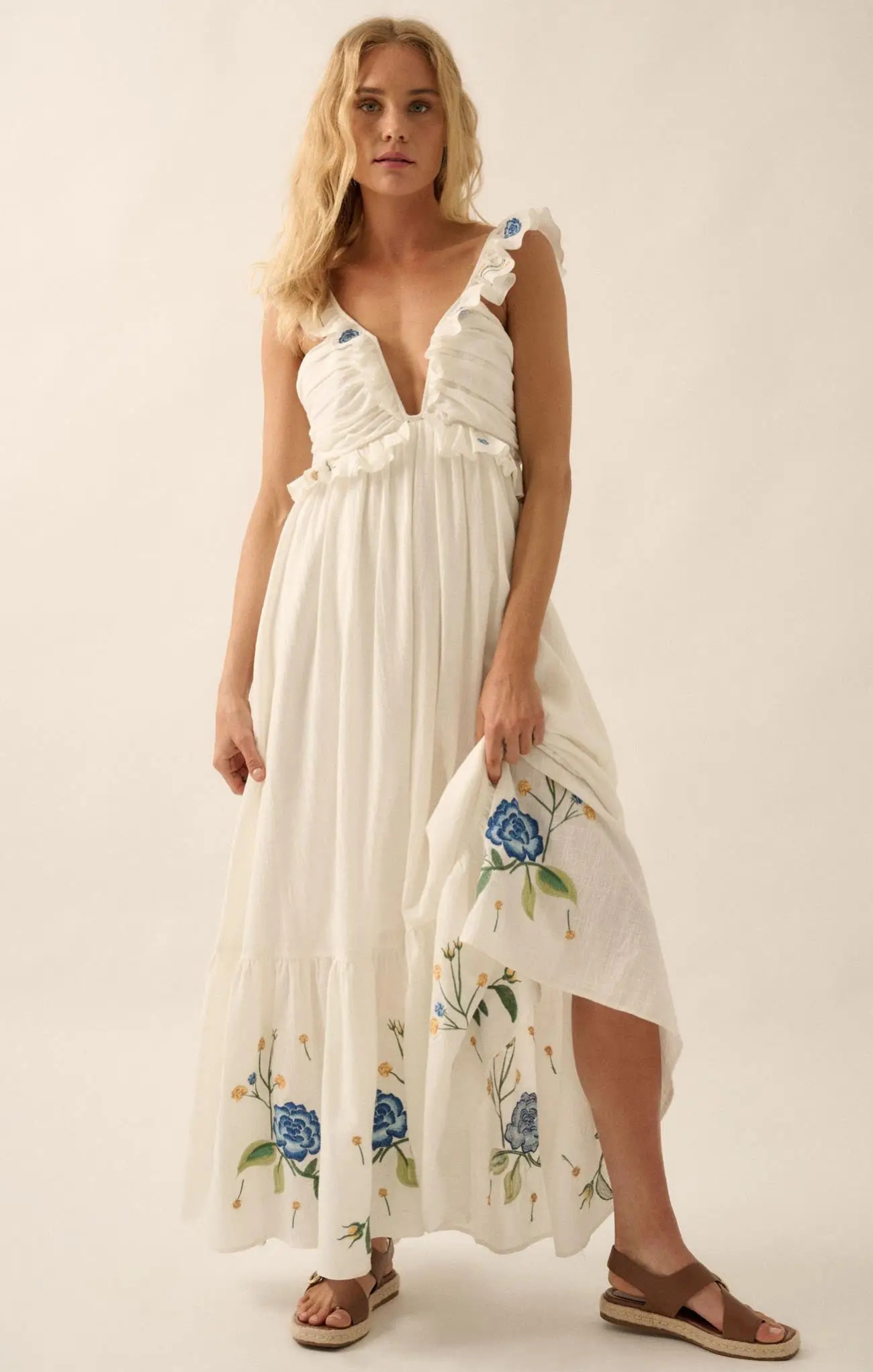 Woman wearing a white dress with floral embroidery on a plain background