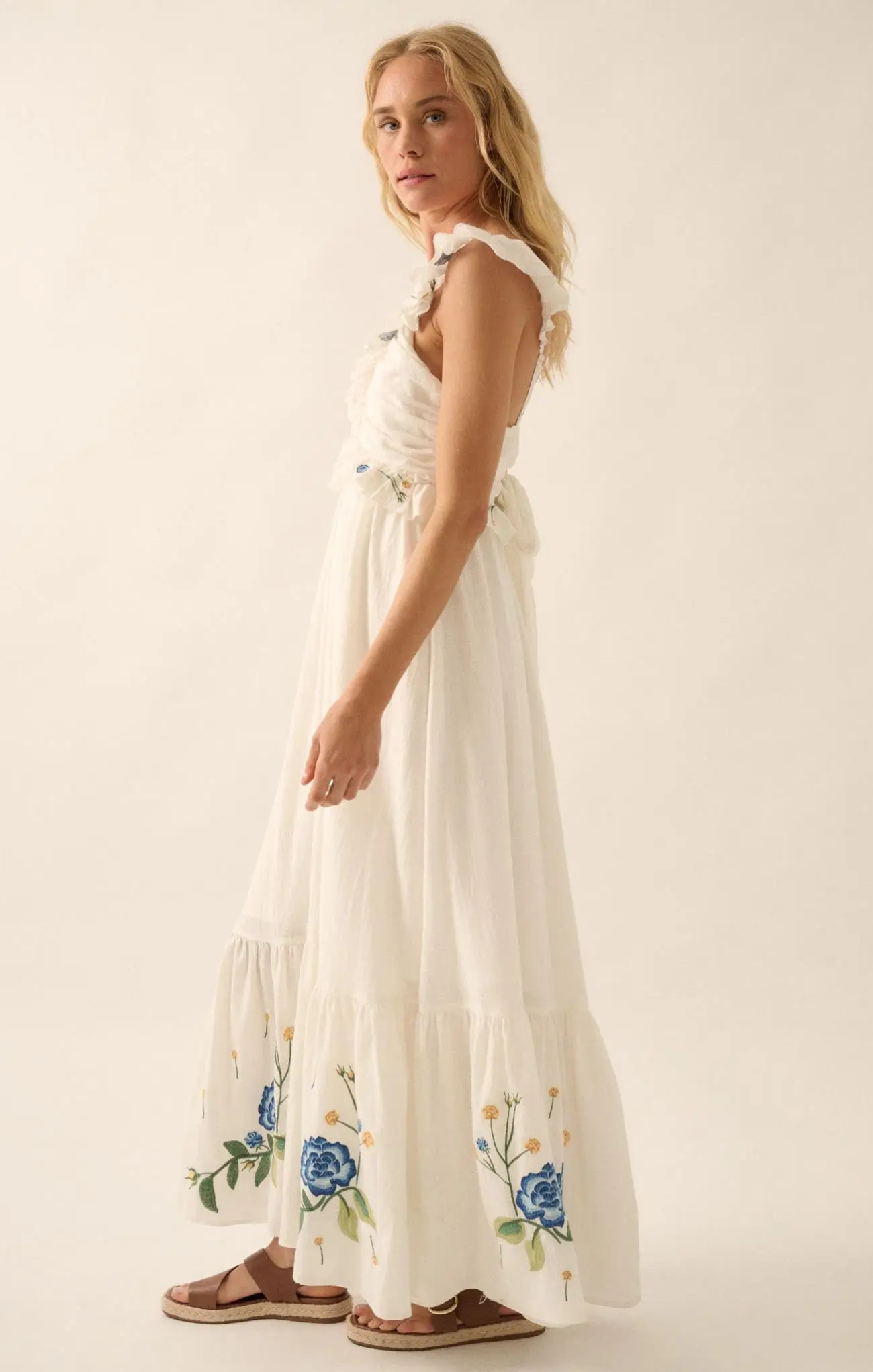 Woman wearing a white dress with floral embroidery on a plain background