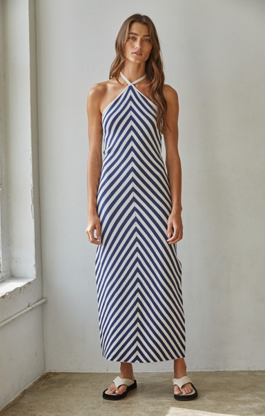 Woman wearing a blue and white striped dress against a plain wall.
