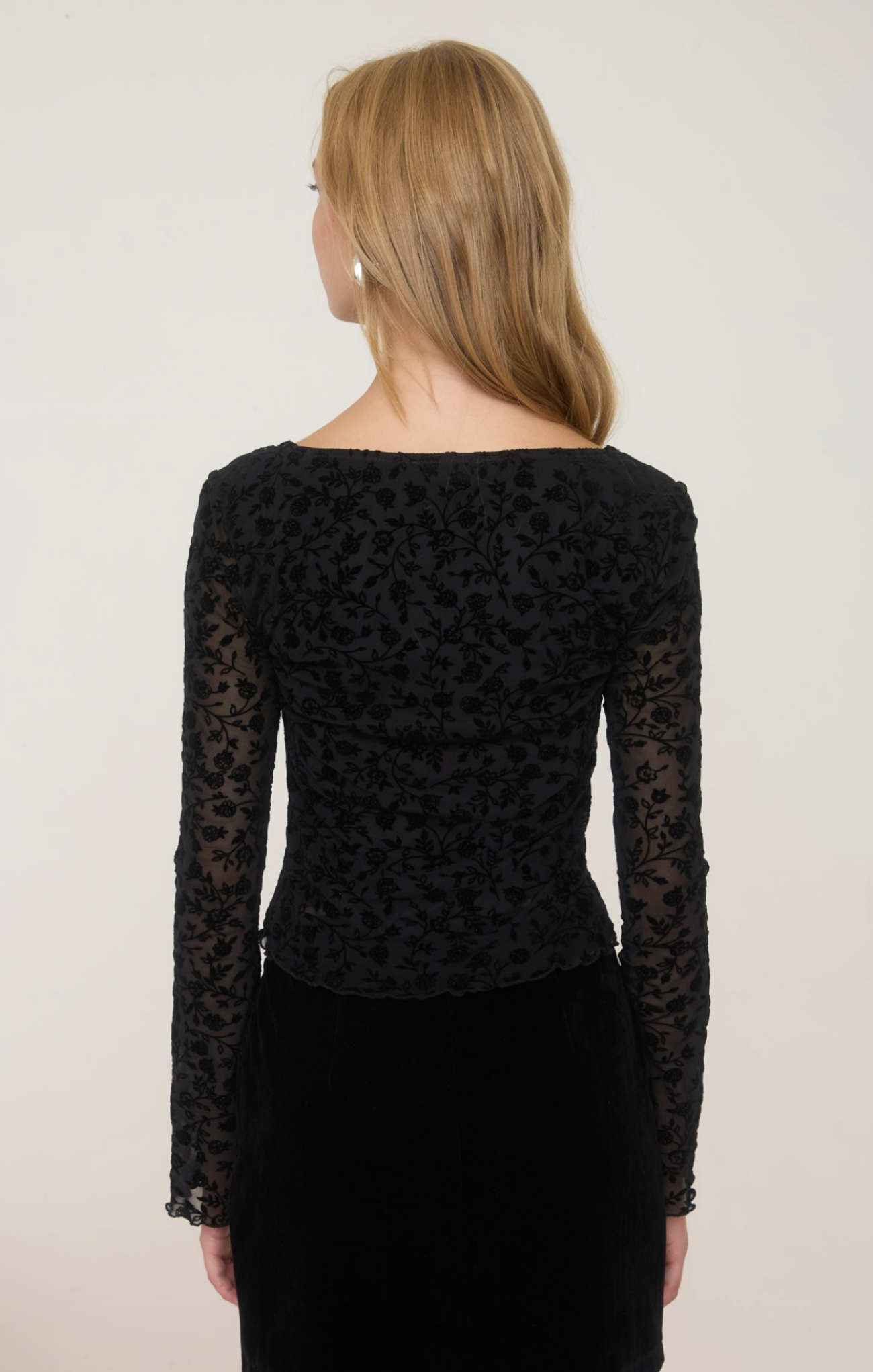 Person wearing a black lace long-sleeve top against a plain background