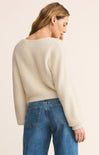 Woman wearing a cream sweater and blue jeans on a beige background