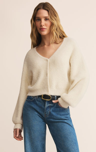 Woman wearing a cream cardigan and blue jeans on a beige background