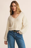 Woman wearing a cream cardigan and blue jeans on a beige background