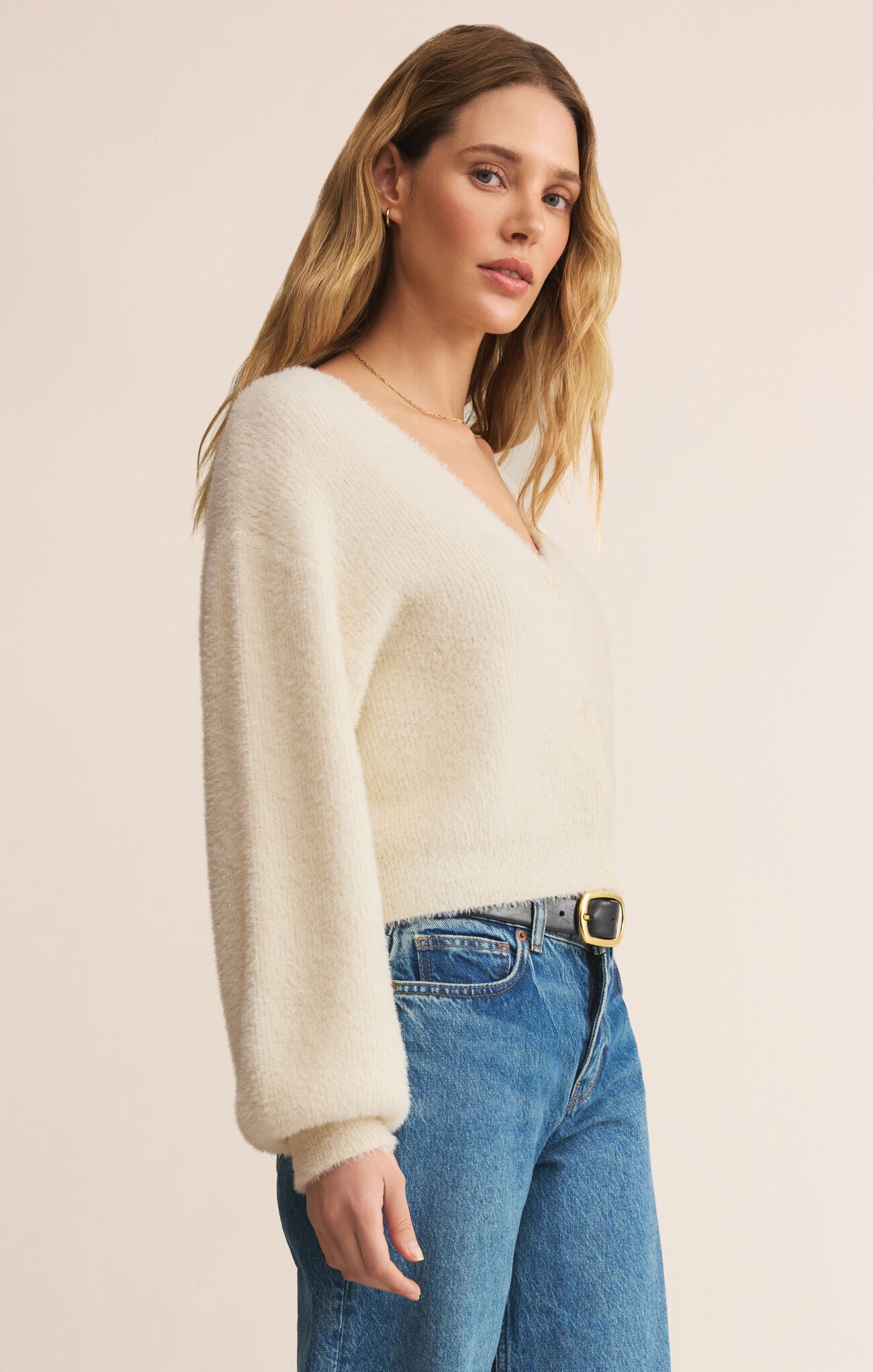 Woman wearing a cream sweater and blue jeans on a beige background