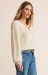 Woman wearing a cream sweater and blue jeans on a beige background