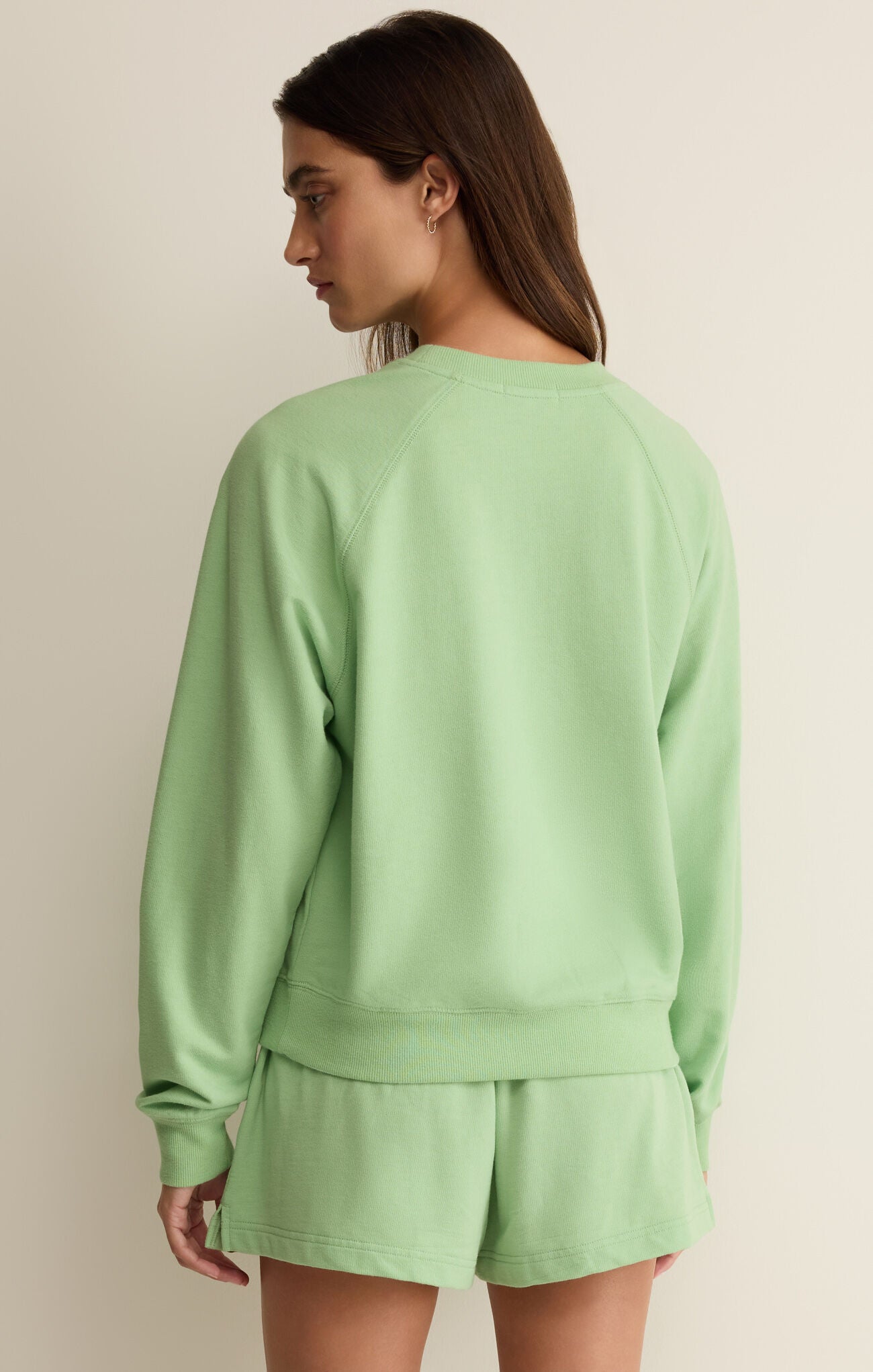 Woman wearing a light green sweatshirt and shorts set on a beige background