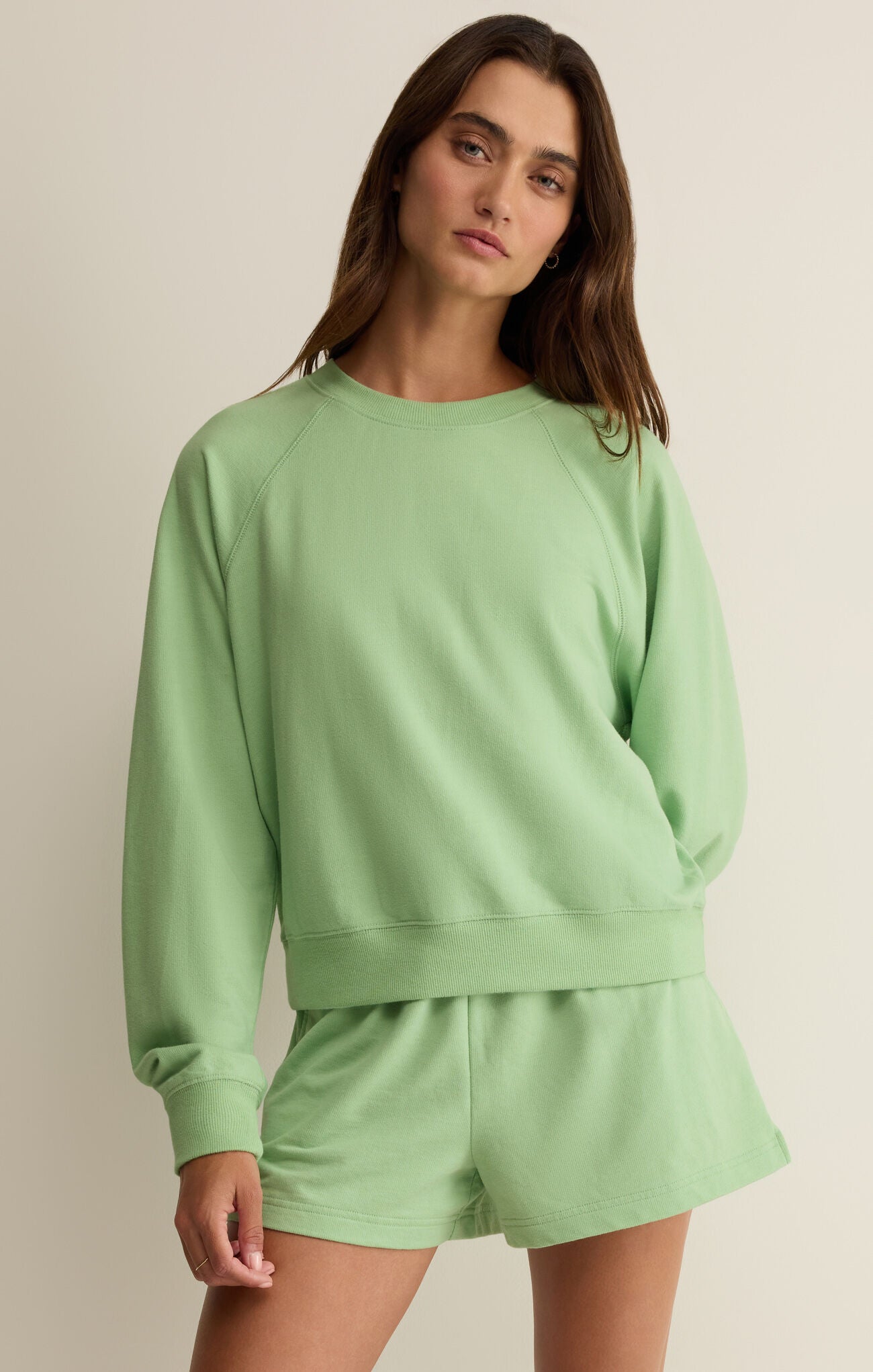 Woman wearing a light green sweatshirt and shorts set against a neutral background