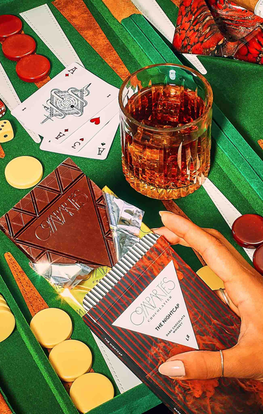 Close-up of a card game with playing cards, chips, and a glass of whiskey on a green table.