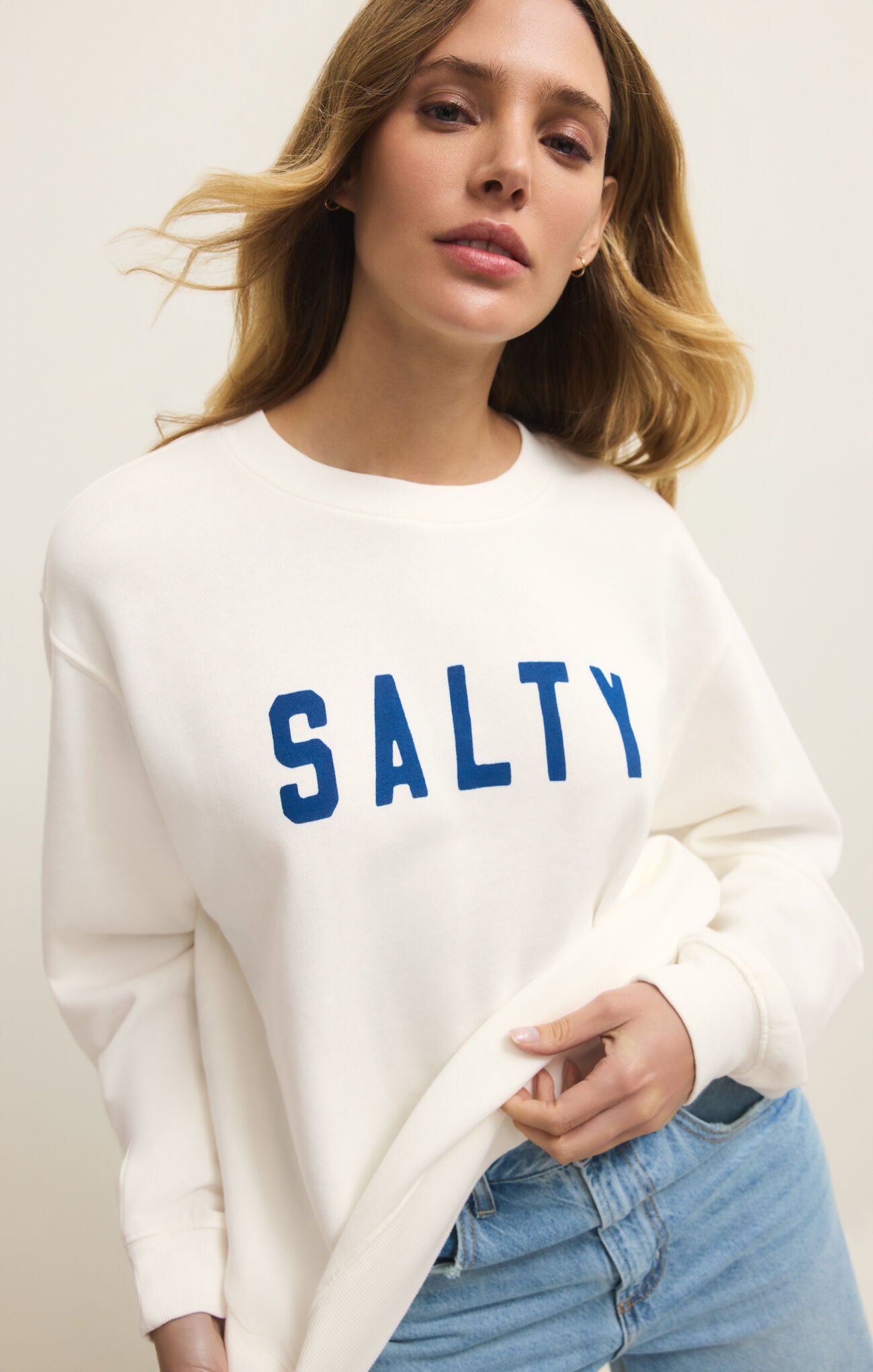 Woman wearing a white sweatshirt with 'SALTY' in blue text on a plain background